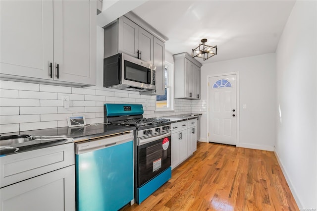 kitchen featuring decorative backsplash, gray cabinets, light wood-type flooring, and appliances with stainless steel finishes