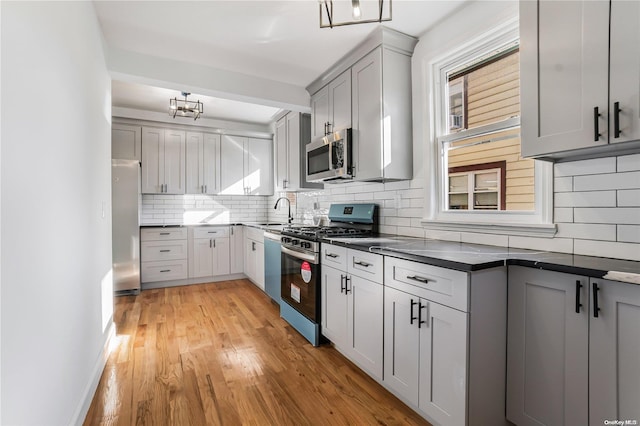 kitchen with decorative backsplash, gray cabinets, light wood-type flooring, and appliances with stainless steel finishes