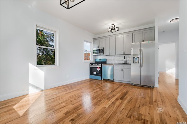 kitchen featuring gray cabinets, light wood-type flooring, backsplash, and appliances with stainless steel finishes