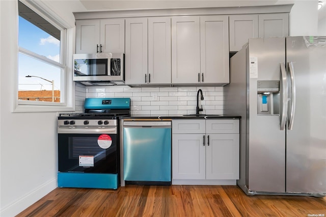 kitchen featuring gray cabinetry, dark wood-type flooring, sink, decorative backsplash, and stainless steel appliances