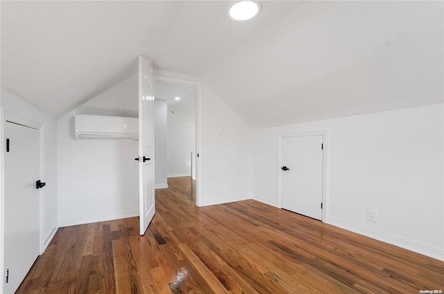 additional living space with a wall unit AC, lofted ceiling, and hardwood / wood-style flooring