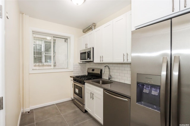 kitchen featuring appliances with stainless steel finishes, backsplash, sink, dark tile patterned flooring, and white cabinetry