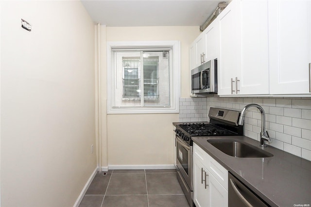 kitchen with decorative backsplash, stainless steel appliances, sink, dark tile patterned flooring, and white cabinets