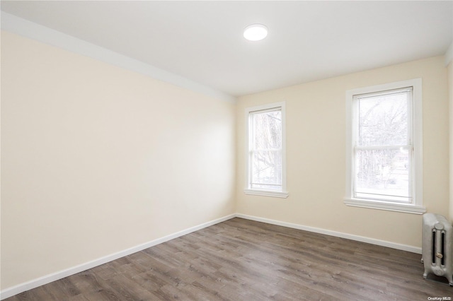 unfurnished room with radiator, hardwood / wood-style floors, and a healthy amount of sunlight