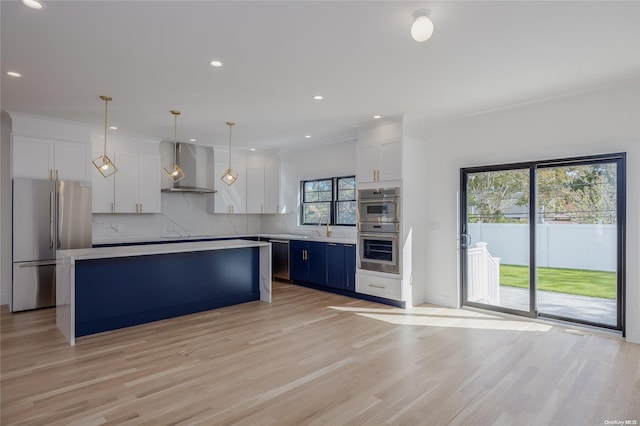 kitchen featuring stainless steel appliances, wall chimney range hood, decorative light fixtures, white cabinets, and a kitchen island