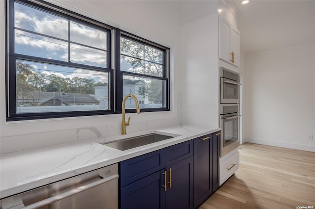 kitchen with sink, stainless steel appliances, light stone counters, light hardwood / wood-style flooring, and white cabinets