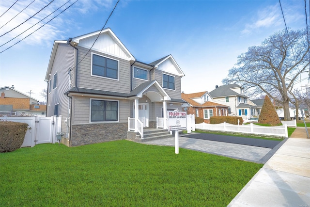 view of front of property featuring driveway, stone siding, a gate, fence, and a front yard