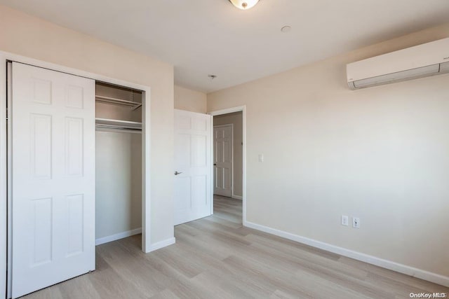 unfurnished bedroom featuring an AC wall unit, a closet, and light hardwood / wood-style flooring