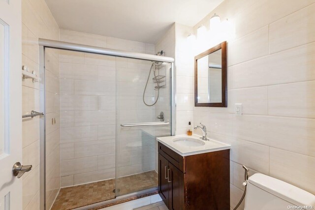 bathroom featuring an enclosed shower, vanity, toilet, and tile walls