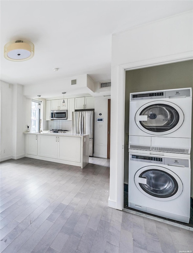 laundry room with light wood-type flooring and stacked washer / drying machine