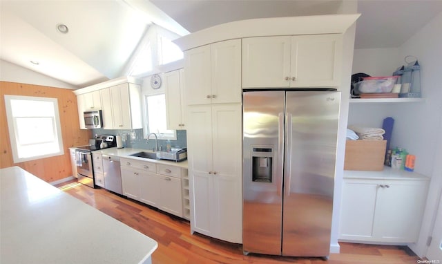 kitchen with light hardwood / wood-style floors, white cabinetry, appliances with stainless steel finishes, and vaulted ceiling