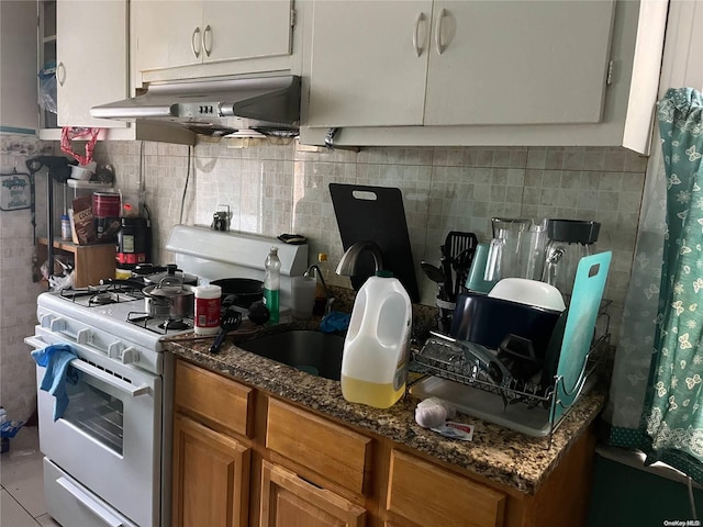 kitchen with dark stone countertops, decorative backsplash, white gas stove, and sink