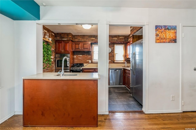 kitchen with dark wood-type flooring, sink, appliances with stainless steel finishes, kitchen peninsula, and brick wall