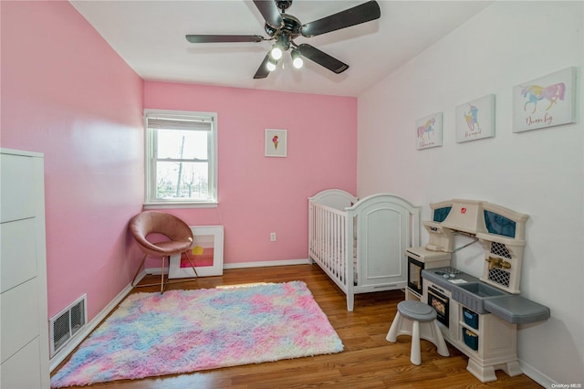 bedroom with ceiling fan, a nursery area, and hardwood / wood-style flooring