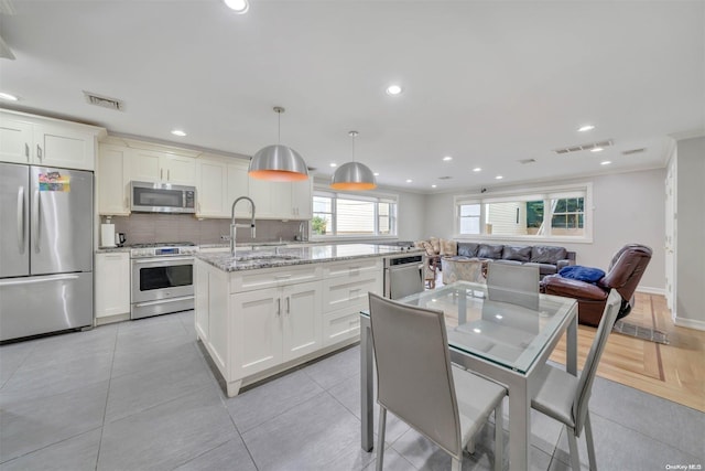 kitchen with backsplash, light stone counters, stainless steel appliances, pendant lighting, and an island with sink