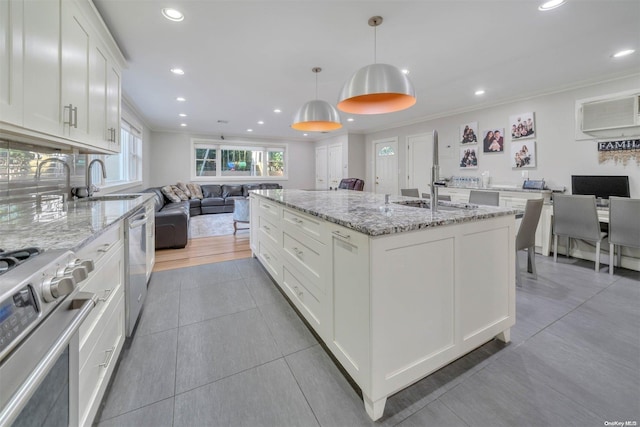 kitchen featuring light stone countertops, pendant lighting, a center island with sink, white cabinets, and appliances with stainless steel finishes