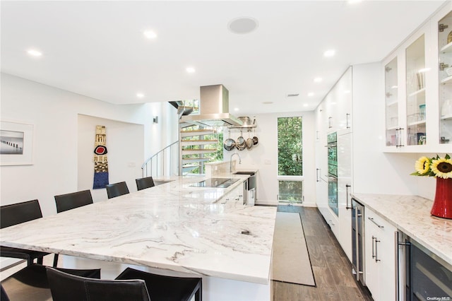 kitchen with white cabinetry, beverage cooler, dark hardwood / wood-style floors, island exhaust hood, and a kitchen bar