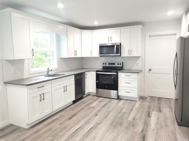 kitchen featuring sink, white cabinetry, appliances with stainless steel finishes, dark stone counters, and light hardwood / wood-style floors