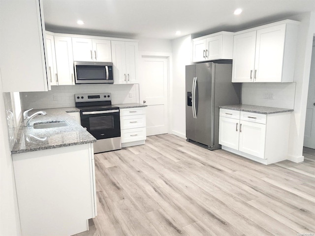 kitchen with sink, white cabinetry, stone countertops, stainless steel appliances, and backsplash