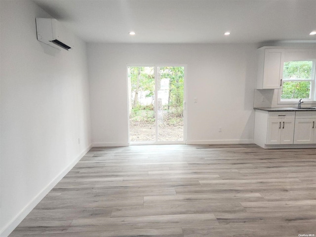 unfurnished dining area with light hardwood / wood-style floors, sink, and an AC wall unit