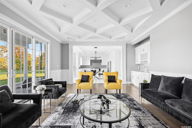 living room featuring beamed ceiling, crown molding, wood-type flooring, coffered ceiling, and sink