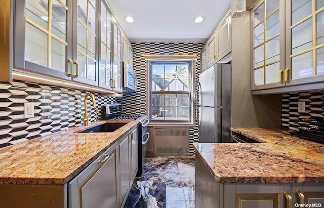 kitchen with sink, decorative backsplash, light stone counters, radiator heating unit, and stainless steel appliances