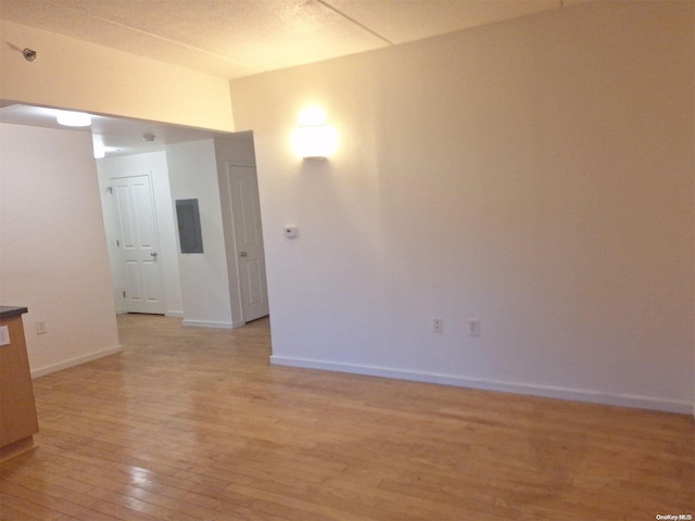 spare room featuring electric panel and light hardwood / wood-style flooring