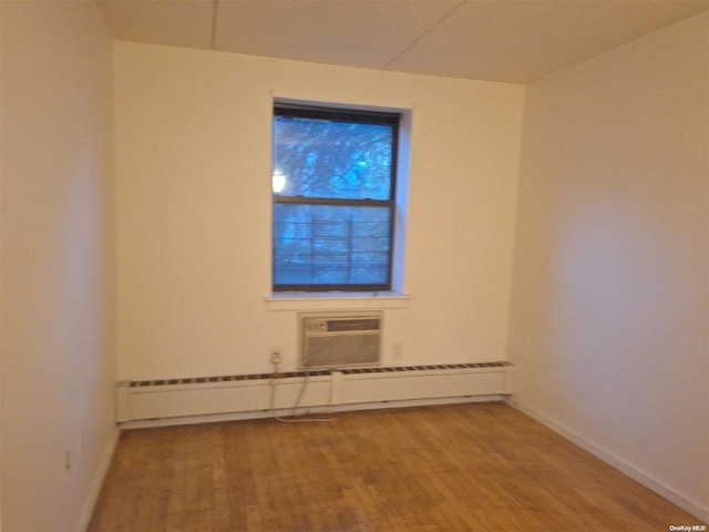 empty room with a wall mounted AC, hardwood / wood-style floors, and baseboard heating