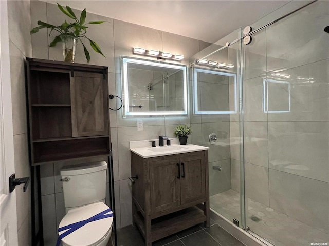 bathroom featuring tile patterned floors, vanity, a shower with door, tile walls, and toilet