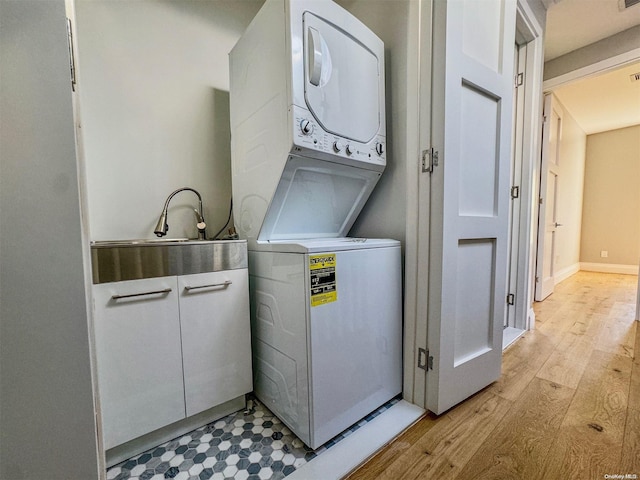 clothes washing area featuring light wood-type flooring, sink, and stacked washer and clothes dryer