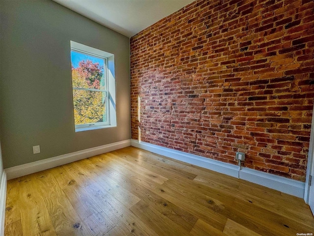 spare room with light hardwood / wood-style floors and brick wall