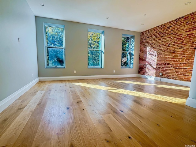 unfurnished room with light wood-type flooring and brick wall