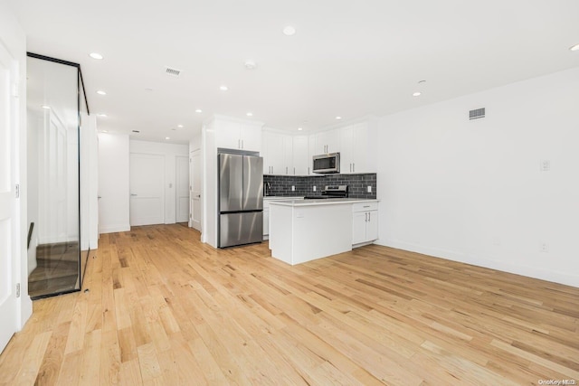 kitchen featuring decorative backsplash, white cabinetry, stainless steel appliances, and light wood-type flooring