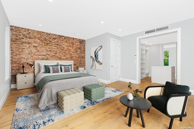 bedroom featuring a closet, a spacious closet, brick wall, and light hardwood / wood-style flooring