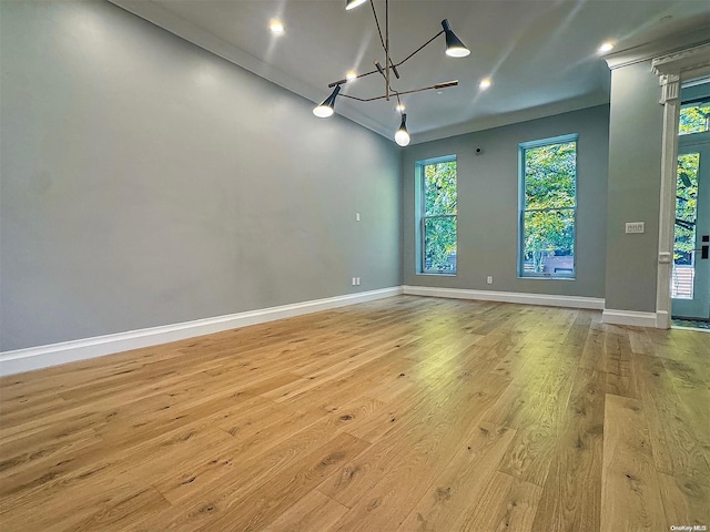 spare room featuring a notable chandelier, light hardwood / wood-style floors, and a healthy amount of sunlight