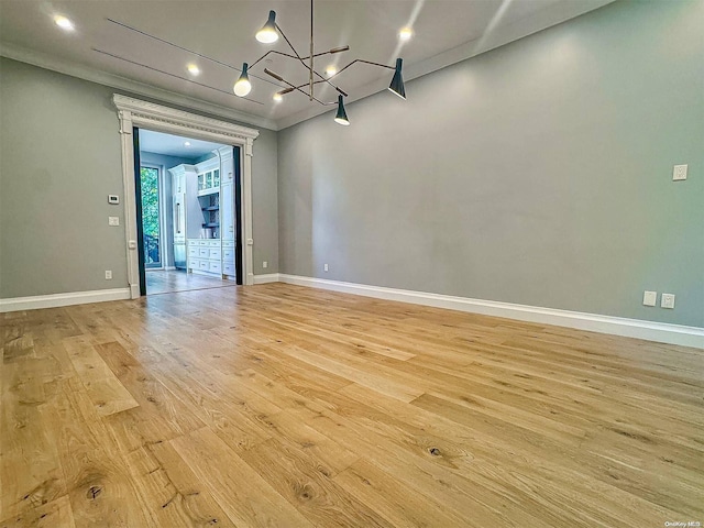 spare room featuring light hardwood / wood-style floors, ornamental molding, and an inviting chandelier