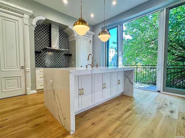 kitchen featuring white cabinets, decorative light fixtures, light stone countertops, and an island with sink