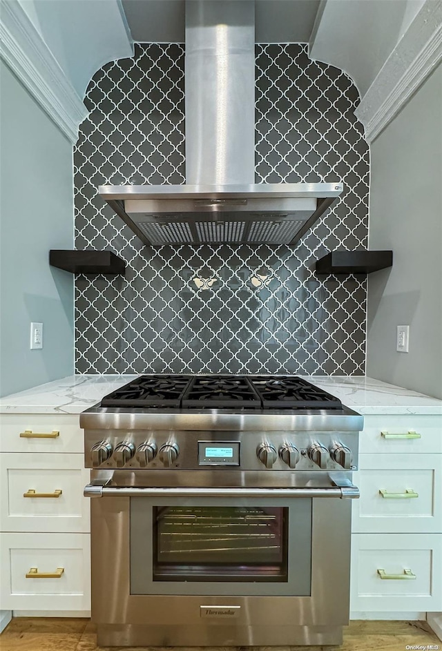 kitchen featuring high end stainless steel range, wall chimney exhaust hood, light stone countertops, tasteful backsplash, and white cabinetry