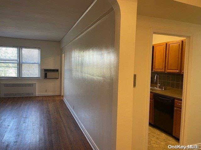 corridor with an AC wall unit, sink, radiator, and light hardwood / wood-style flooring