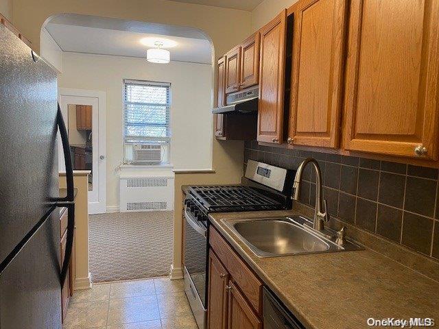 kitchen featuring appliances with stainless steel finishes, backsplash, sink, light tile patterned floors, and radiator heating unit