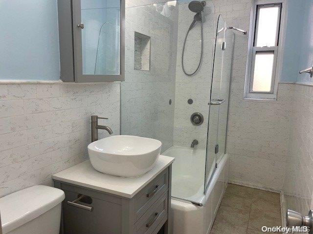 full bathroom featuring tile patterned floors, bath / shower combo with glass door, vanity, tile walls, and toilet