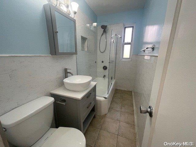 full bathroom with combined bath / shower with glass door, tile patterned floors, vanity, tile walls, and toilet