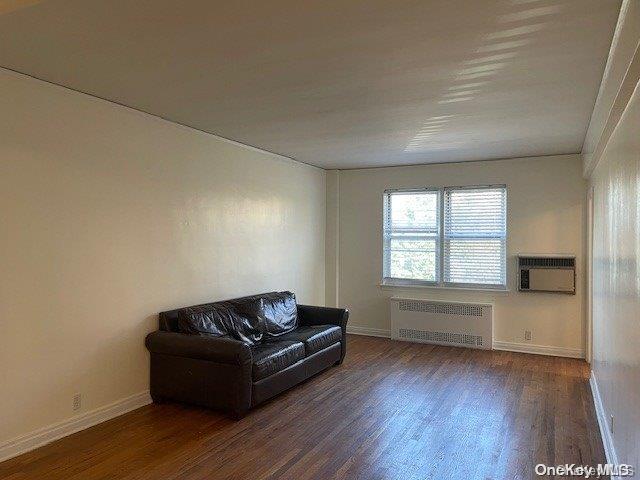 living area with radiator heating unit, dark wood-type flooring, and an AC wall unit