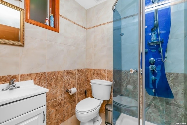 bathroom with vanity, a shower with door, toilet, and tile walls