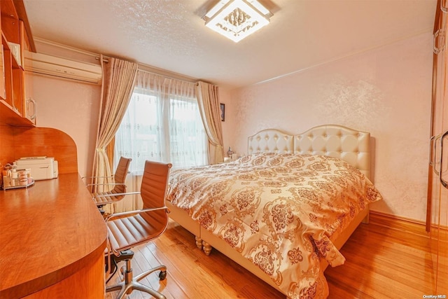 bedroom featuring hardwood / wood-style floors, a textured ceiling, and a wall mounted AC