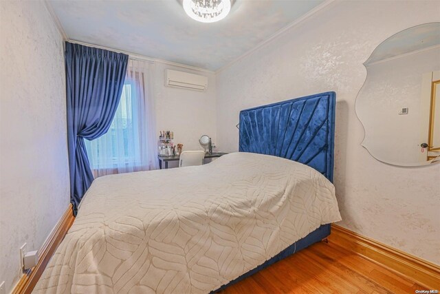 bedroom featuring hardwood / wood-style floors, ornamental molding, and a wall mounted air conditioner