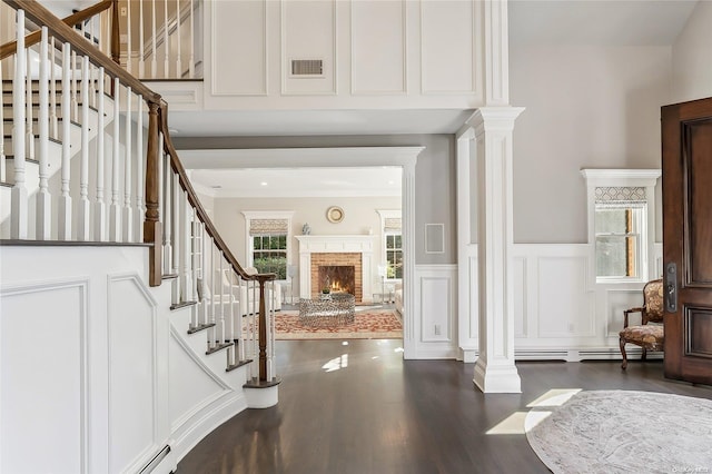 foyer entrance with a fireplace, a baseboard heating unit, decorative columns, and dark wood-type flooring