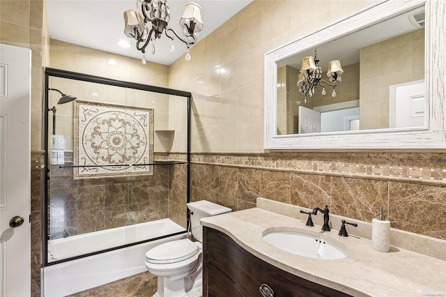 full bathroom featuring combined bath / shower with glass door, a chandelier, toilet, vanity, and tile walls