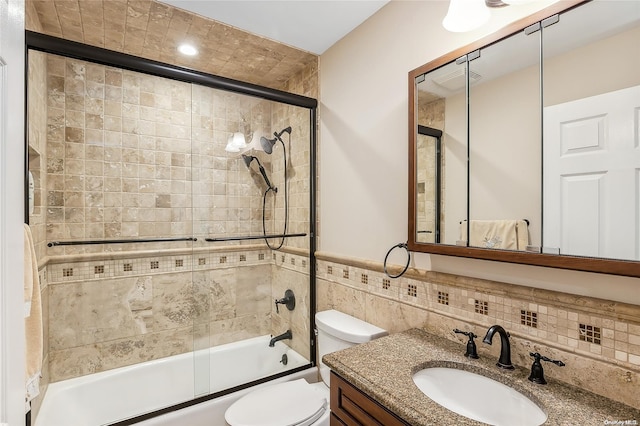 full bathroom featuring toilet, vanity, tile walls, and combined bath / shower with glass door