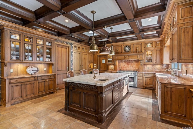 kitchen featuring coffered ceiling, a center island with sink, stainless steel stove, beamed ceiling, and light stone counters